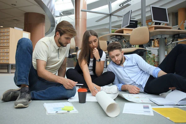 Groep van jonge ondernemers en ontwerpers kijken naar projectplan aangelegd op verdieping. Ze werken aan nieuw project. — Stockfoto