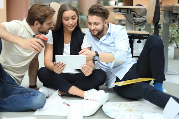 Grupo de jóvenes empresarios y diseñadores que miran el plan de proyecto dispuesto en el piso. Están trabajando en un nuevo proyecto . — Foto de Stock