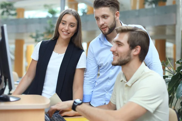 Gruppo di giovani in abbigliamento casual seduti alla scrivania dell'ufficio e discutere di qualcosa mentre guardano il PC insieme . — Foto Stock