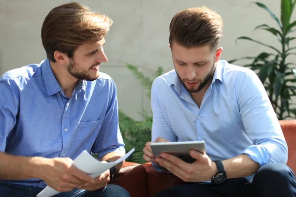 Mogen affärsman använder en digital surfplatta för att diskutera information med en yngre kollega i ett modernt kontor. — Stockfoto