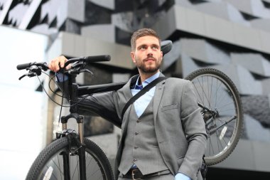 Kendine güvenen genç işadamı açık havada yürürken onun bisiklet taşıma.