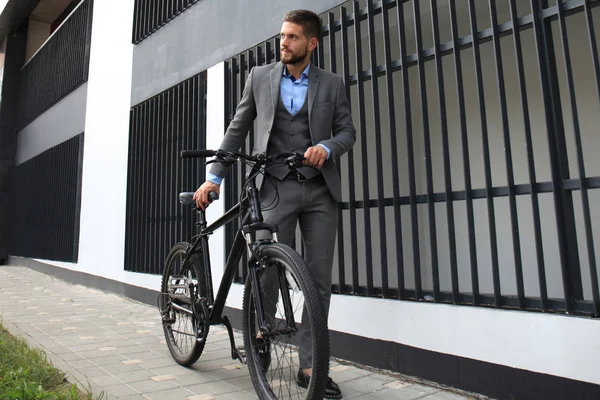 Jovem empresário confiante de pé com bicicleta na rua da cidade . — Fotografia de Stock