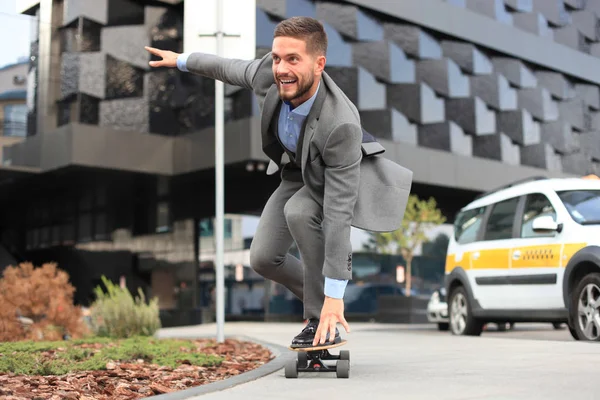 Jistý mladý podnikatel v oboru oblek na longboard spěchal do své pracovny, na ulici ve městě — Stock fotografie