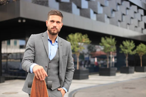 Jovem empresário confiante andando na rua, usando longboard . — Fotografia de Stock