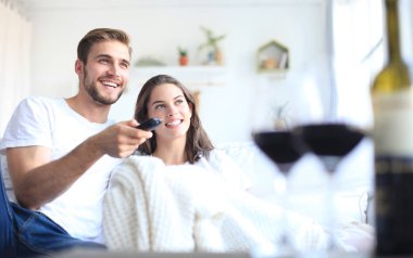 Seven çift kanepe evde genç tv izlerken ve gülüyor, bir kadeh kırmızı şarap içmek.