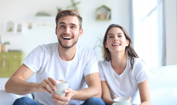 Jong liefhebbend paar op de bank thuis kijken tv en lachen. — Stockfoto