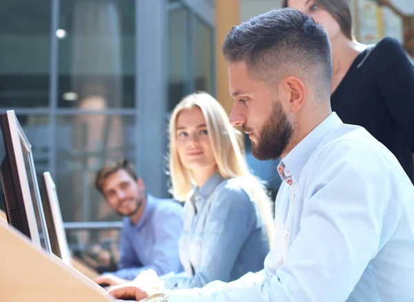 Grupo de jóvenes en ropa casual sentados en el escritorio de la oficina y discutiendo algo mientras miran PC juntos . — Foto de Stock