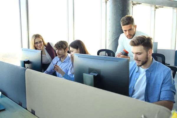 Grupo de jóvenes en ropa casual sentados en el escritorio de la oficina y discutiendo algo mientras miran PC juntos . —  Fotos de Stock