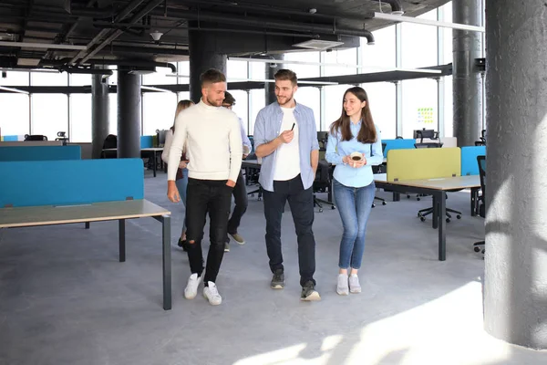 Longitud completa de los jóvenes en ropa casual inteligente discutiendo negocios y sonriendo mientras caminan por la oficina . — Foto de Stock