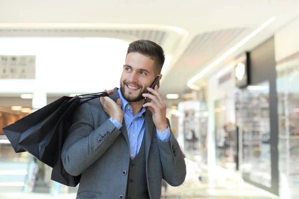 Młody biznesmen z torbą na zakupy rozmawia przez telefon w pomieszczeniu. — Zdjęcie stockowe