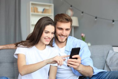 Genç çift evdeki kanepede oturmuş akıllı bir telefonla online içeriği izliyorlar..
