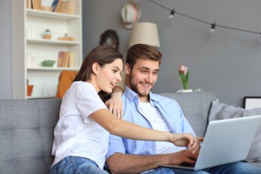 Genç çift evde bazı online alışveriş yapıyor, kanepede bir dizüstü bilgisayar kullanarak.