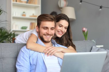 Genç çift evde bazı online alışveriş yapıyor, kanepede bir dizüstü bilgisayar kullanarak.