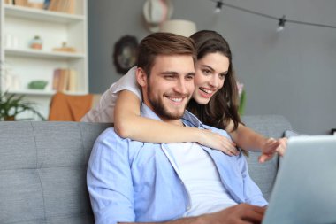Genç çift evde bazı online alışveriş yapıyor, kanepede bir dizüstü bilgisayar kullanarak.