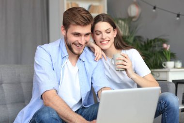 Genç çift evde bazı online alışveriş yapıyor, kanepede bir dizüstü bilgisayar kullanarak.