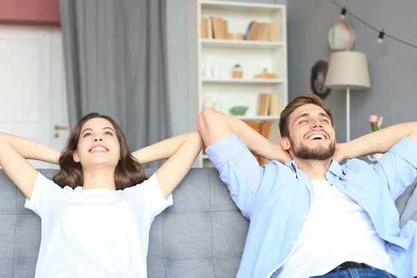 Sonriendo hermosa pareja sentada en un sofá y soñando con un nuevo hogar. —  Fotos de Stock
