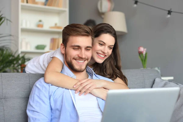 Pareja joven haciendo algunas compras en línea en casa, utilizando un ordenador portátil en el sofá . —  Fotos de Stock