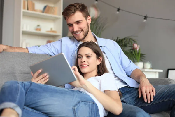 Молода пара дивиться медіаконтент онлайн в планшеті, сидячи на дивані у вітальні . — стокове фото