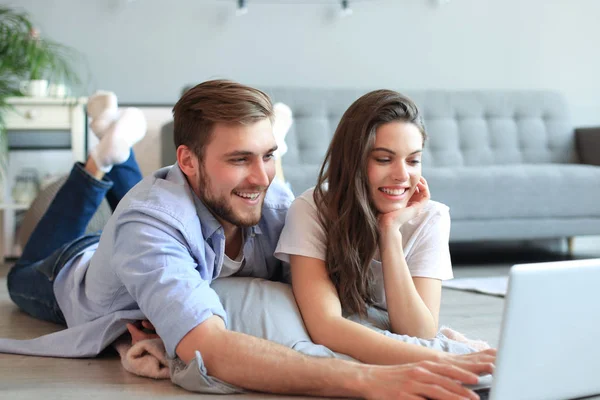 Giovane coppia fare un po 'di shopping online a casa, utilizzando un computer portatile sul pavimento . — Foto Stock