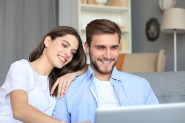 Genç çift evde bazı online alışveriş yapıyor, kanepede bir dizüstü bilgisayar kullanarak.