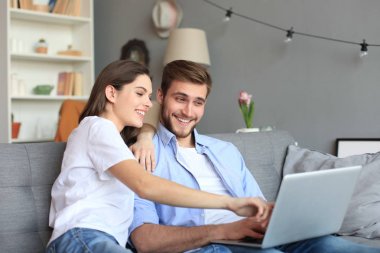 Genç çift evde bazı online alışveriş yapıyor, kanepede bir dizüstü bilgisayar kullanarak.