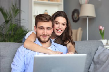 Genç çift evde bazı online alışveriş yapıyor, kanepede bir dizüstü bilgisayar kullanarak.
