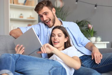 Genç bir çift, oturma odasındaki kanepede oturup internetten medya içeriğini izliyor..