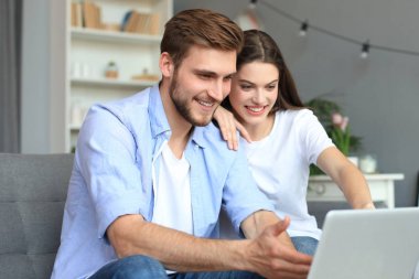 Genç çift evde bazı online alışveriş yapıyor, kanepede bir dizüstü bilgisayar kullanarak.