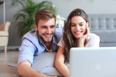 Genç çift evde bazı online alışveriş yapıyor, katta bir laptop kullanarak.