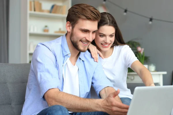 Pareja joven haciendo algunas compras en línea en casa, utilizando un ordenador portátil en el sofá . —  Fotos de Stock