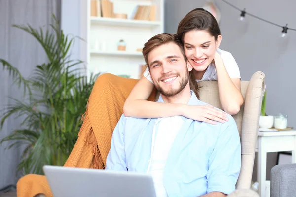 Casal jovem fazendo algumas compras on-line em casa, usando um laptop no sofá . — Fotografia de Stock
