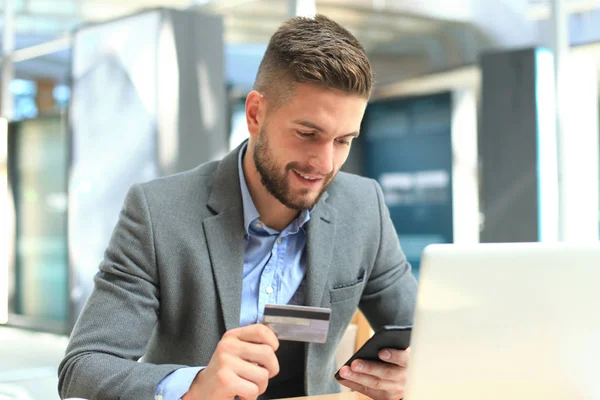 Feliz joven hombre de negocios utilizando el ordenador portátil y la tarjeta de crédito en la mesa . — Foto de Stock