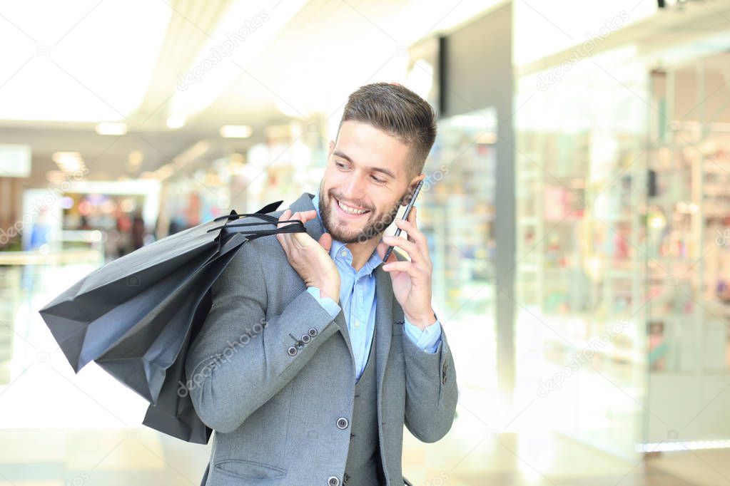 Young businessman with shopping bag talking on the phone indoors.