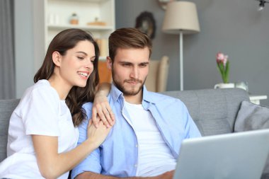 Genç çift evde bazı online alışveriş yapıyor, kanepede bir dizüstü bilgisayar kullanarak.