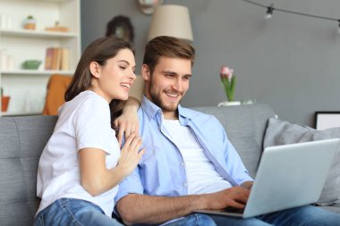 Genç çift evde bazı online alışveriş yapıyor, kanepede bir dizüstü bilgisayar kullanarak.