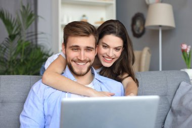 Genç çift evde bazı online alışveriş yapıyor, kanepede bir dizüstü bilgisayar kullanarak.
