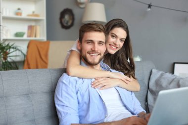 Genç çift evde bazı online alışveriş yapıyor, kanepede bir dizüstü bilgisayar kullanarak.