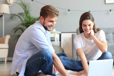 Genç çift evde bazı online alışveriş yapıyor, katta bir laptop kullanarak.