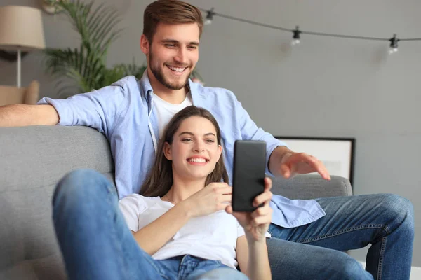 Молода пара дивиться онлайн-контент в смартфоні, сидячи на дивані вдома у вітальні . — стокове фото