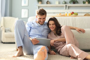 Pijamalı genç bir çift oturma odasındaki tablette oturmuş medyanın içeriğini izliyorlar..