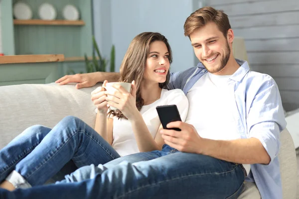Genç çift evdeki kanepede oturmuş akıllı bir telefonla online içeriği izliyorlar..