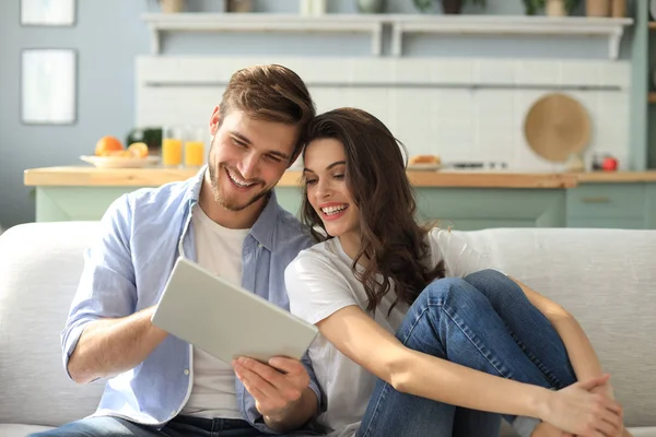 Giovane coppia che guarda contenuti multimediali online in un tablet seduto su un divano in soggiorno. — Foto Stock