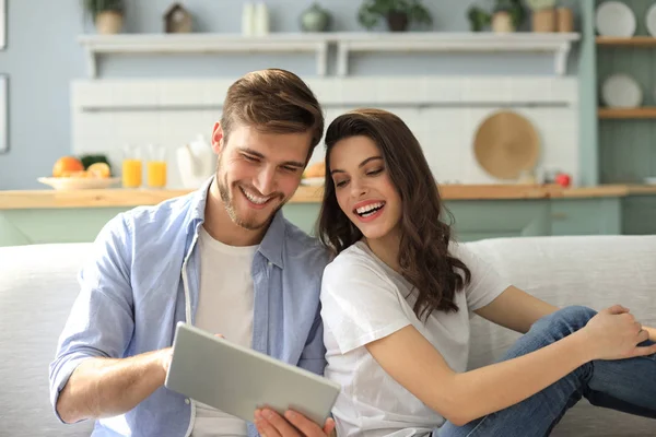 Jong stel kijken media-inhoud online in een tablet zitten op een bank in de woonkamer. — Stockfoto