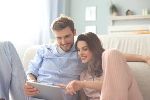 Pareja joven en pijama viendo contenido multimedia en línea en una tableta sentada en el suelo en la sala de estar. —  Fotos de Stock