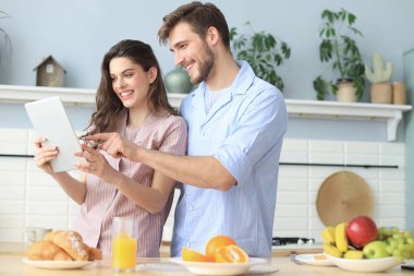 Pijama mutlu genç çift bir tablet online içerik izlerken ve evde mutfakta yemek yaparken gülümseyerek.