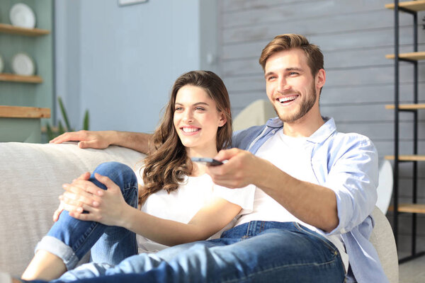 Young loving couple on sofa at home watching tv and laughing.