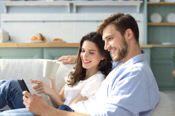 Pasangan muda menonton konten online dalam ponsel pintar duduk di sofa di rumah di ruang tamu. — Stok Foto