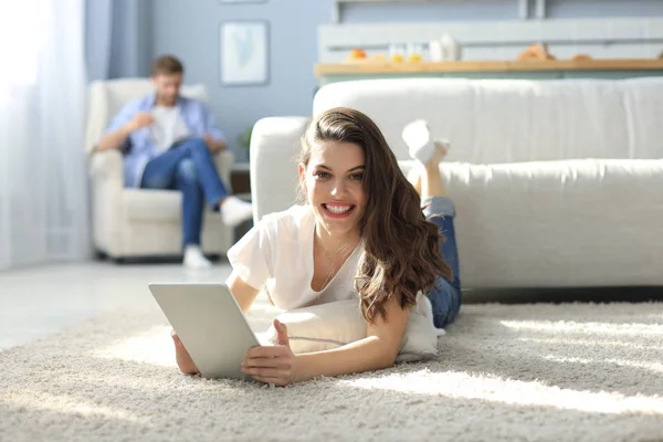 Sonriendo hermosa mujer usando el ordenador portátil con el hombre borroso en el fondo en casa . —  Fotos de Stock