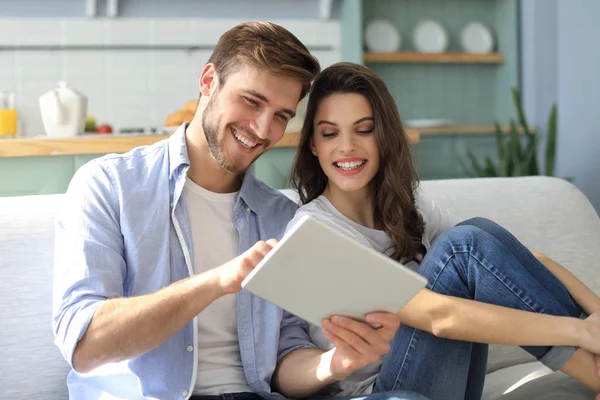 Jovem casal assistindo conteúdo de mídia on-line em um tablet sentado em um sofá na sala de estar. — Fotografia de Stock