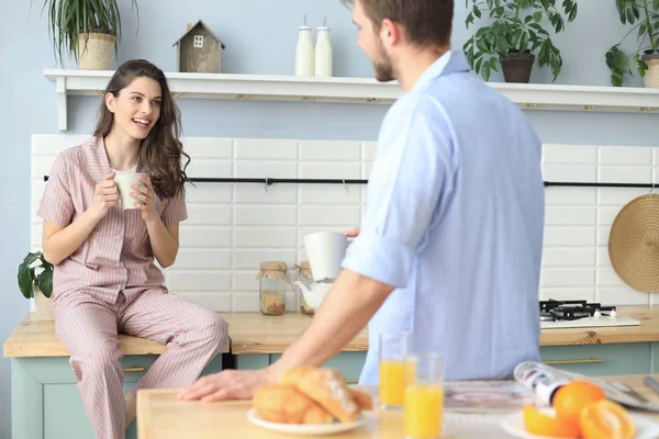 Hermosa pareja joven en pijama se mira y sonríe mientras cocina en casa. —  Fotos de Stock